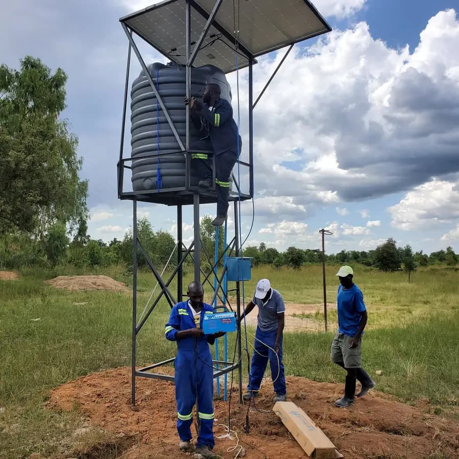 Two water tanks on a tall steel stand with a solar panel above, crew in blue overalls working below