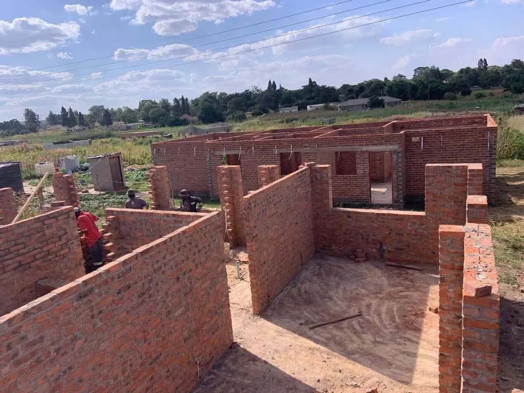 Red brick walls of a house under construction, built up to window height with a worker inside