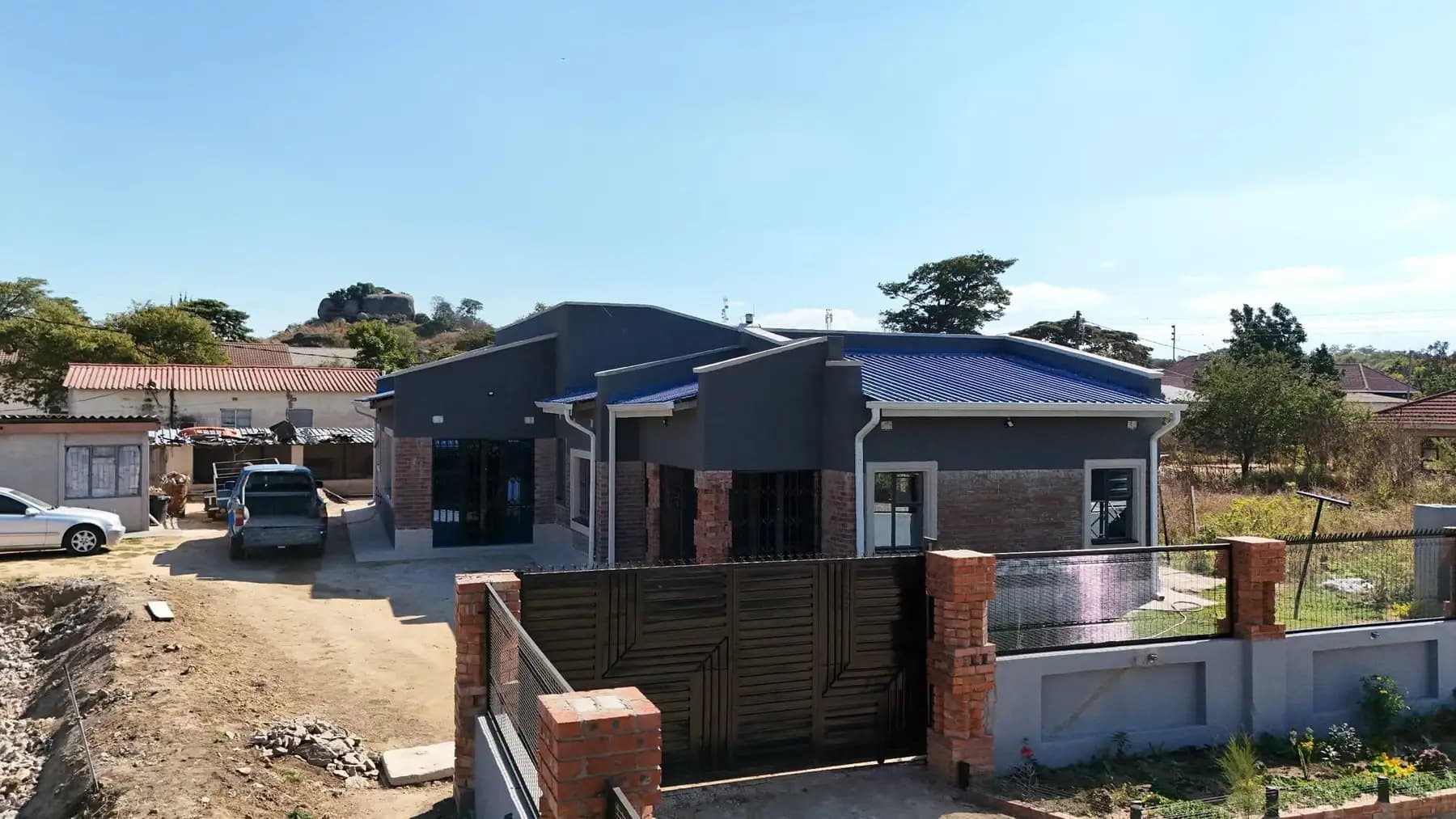 A finished modern house behind brick gate piers and a steel driveway gate