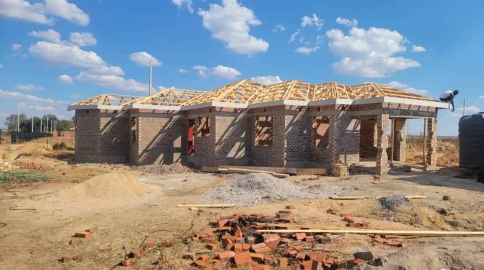 Timber roof trusses erected over a brick house under construction, bricks stacked below