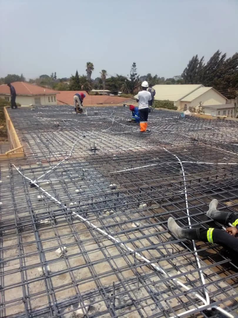 Workers levelling wet concrete over reinforcement mesh across a large ground slab