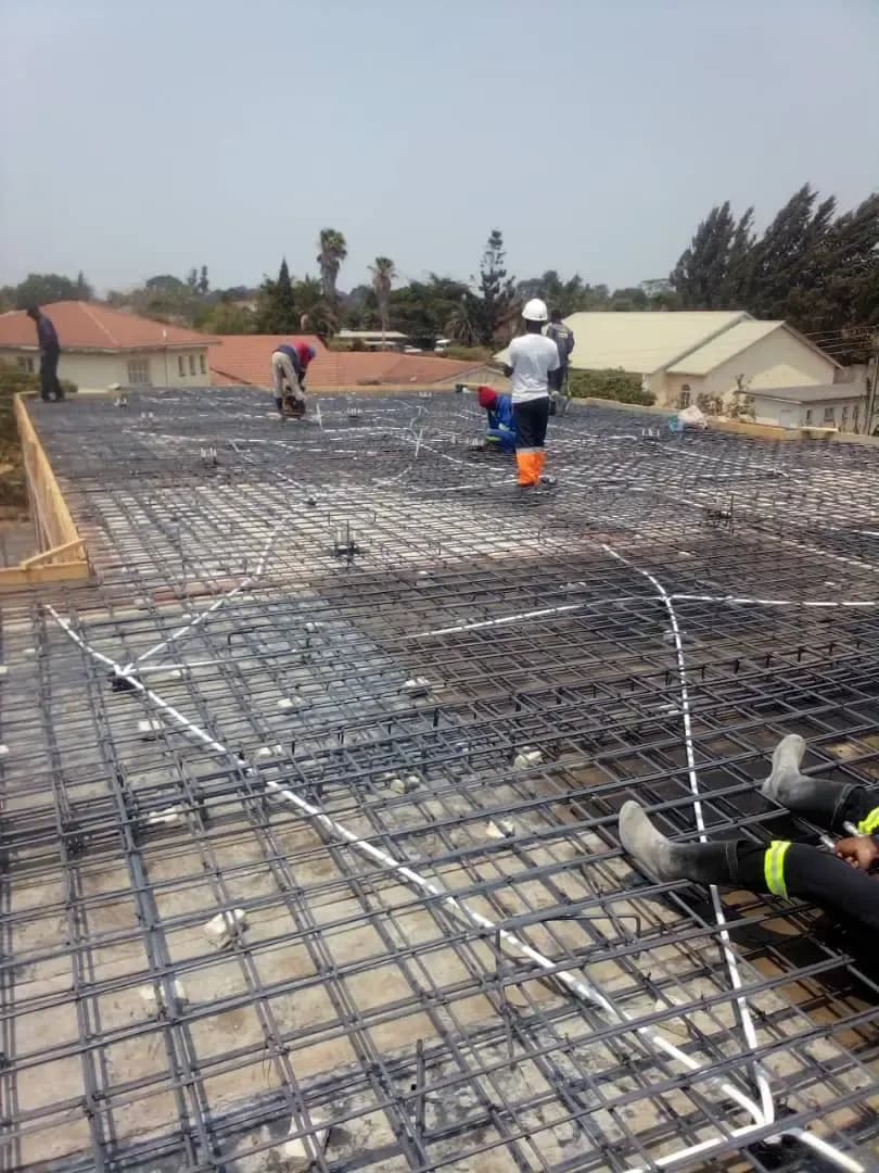 Workers levelling wet concrete over reinforcement mesh across a large ground slab