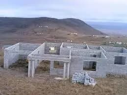 A grey block building under construction on a hillside, with columns cast and a mountain behind