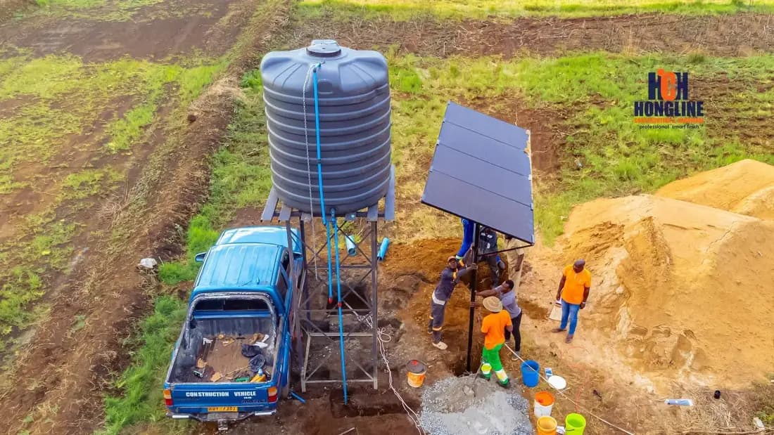 A water tank on a raised stand beside a solar panel, with the crew and their truck alongside