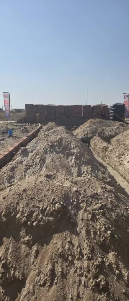 A long red brick boundary wall with heaps of sand piled in front of it