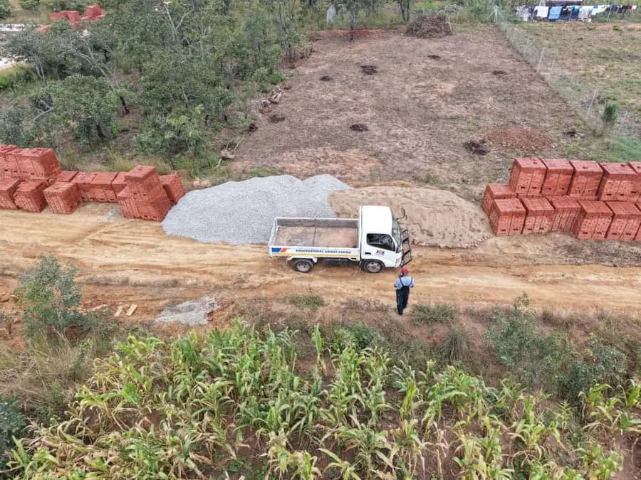Aerial view of a small tipper truck between stacks of brick and a heap of stone on open ground
