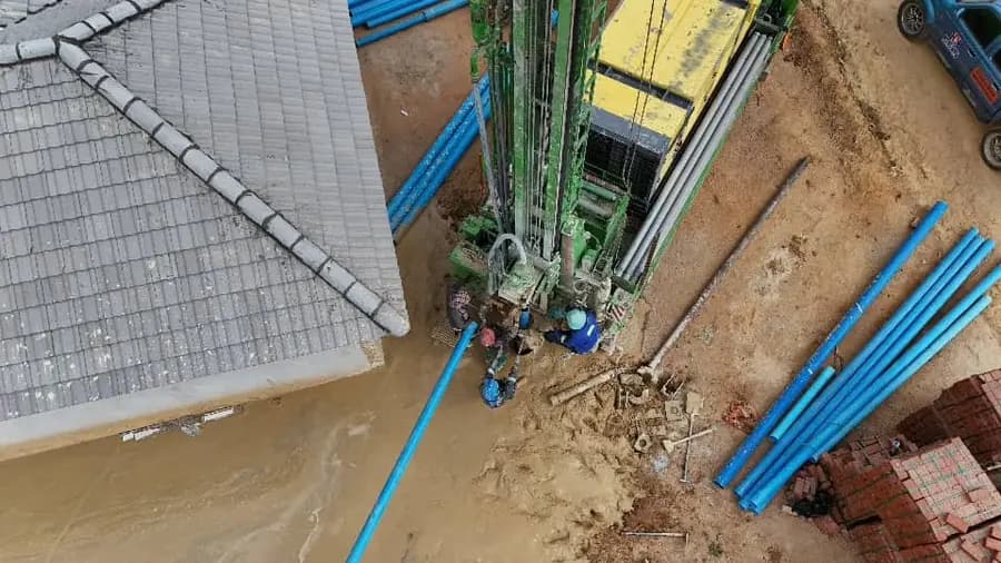 Close aerial view of a drilling rig mast over the hole, blue casing pipe and muddy return water on the ground