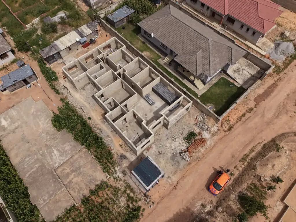 Aerial view of block walls at floor level on a house under construction, with a completed roof behind