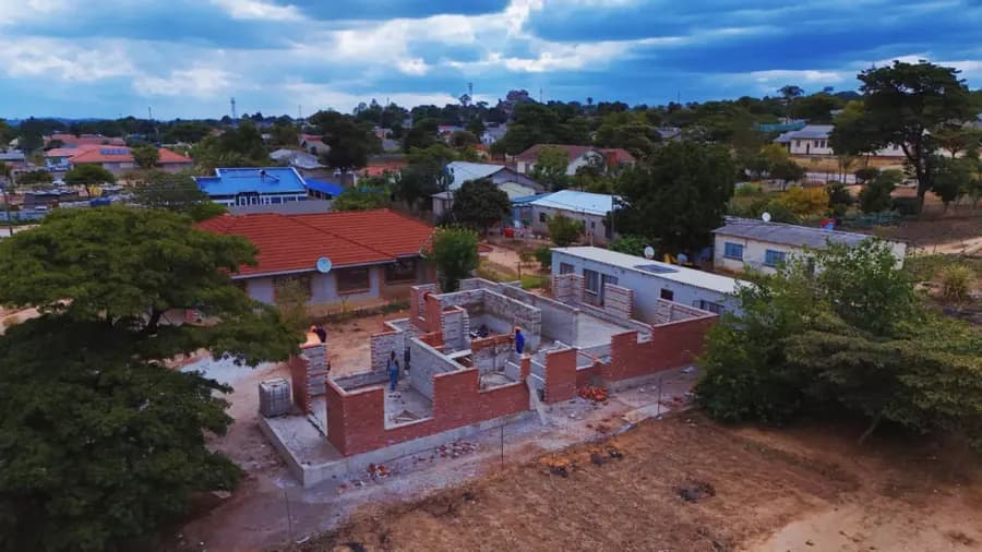 Aerial view of a brick house under construction among finished houses in a leafy suburb