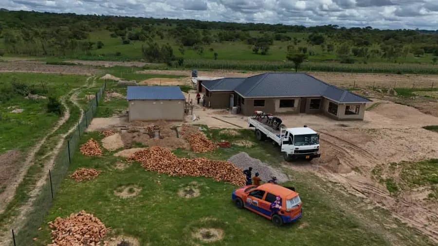 Aerial view of a finished single-storey house with a dark roof, a delivery truck and a bakkie parked on the plot