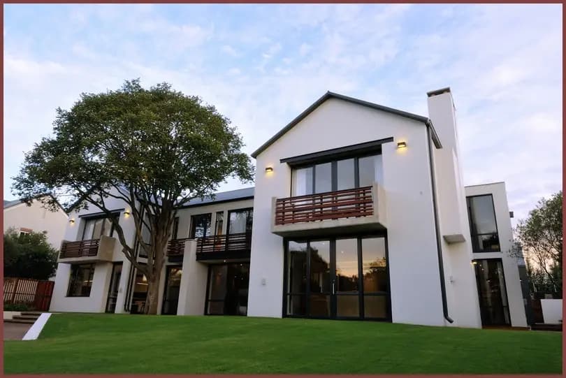 A completed two-storey white house with large aluminium-framed windows and a first-floor balcony