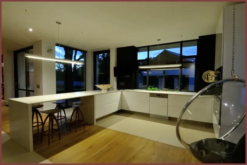 A modern white kitchen with an island, timber floor and wide windows onto the garden