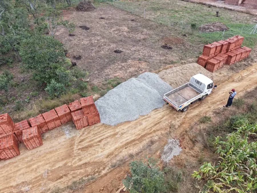 Aerial view of brick stacks and a stone heap beside a small truck on a cleared plot