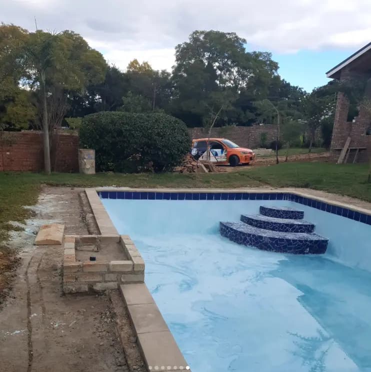 A swimming pool in a walled garden with tiled steps and mature trees behind