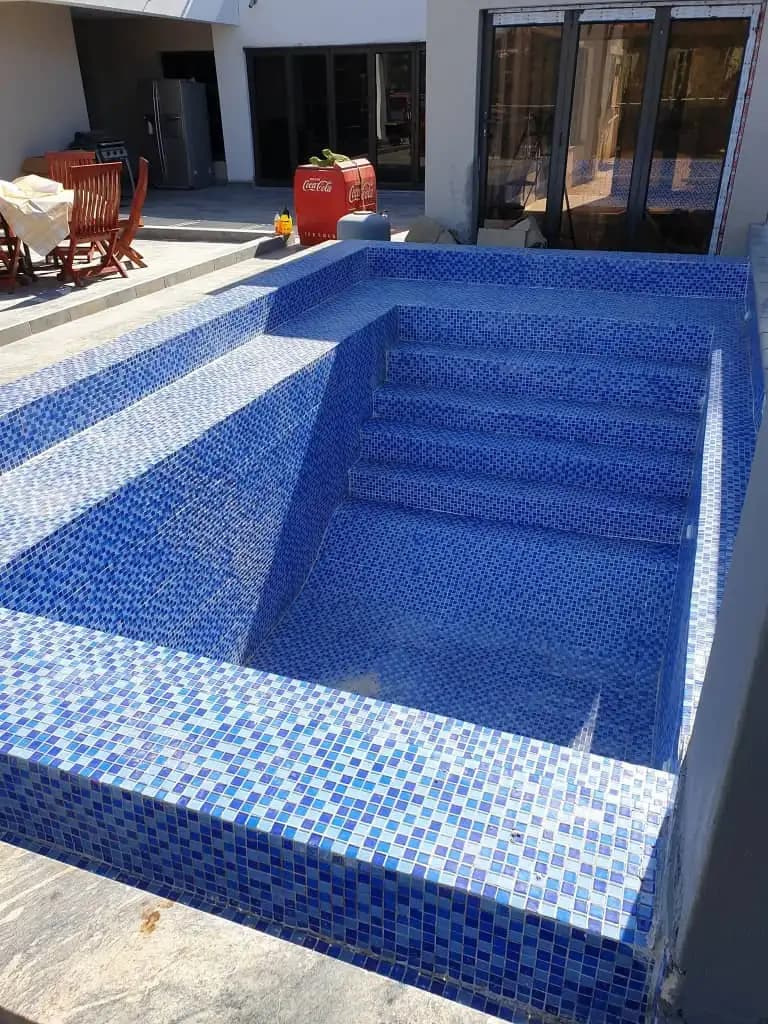 A swimming pool finished in blue mosaic tile, with steps down into the shallow end