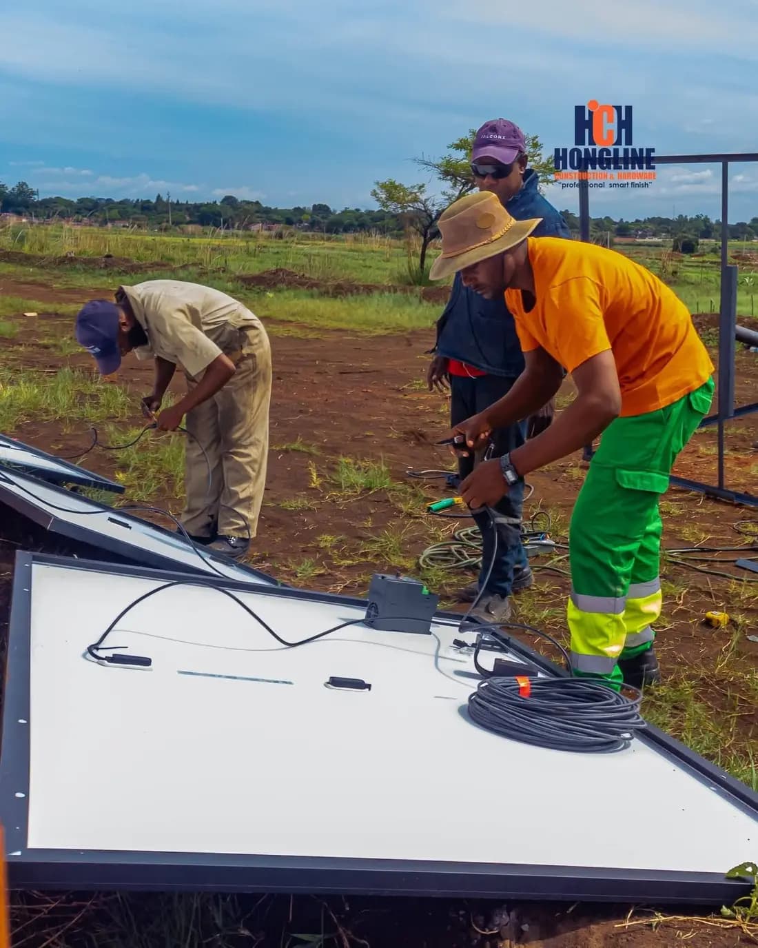 Two workers fitting a solar panel on site, with a Hongline banner strung on the fence behind them