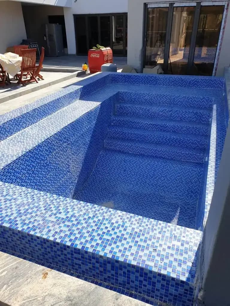 A swimming pool finished in blue mosaic tile, with steps down into the shallow end