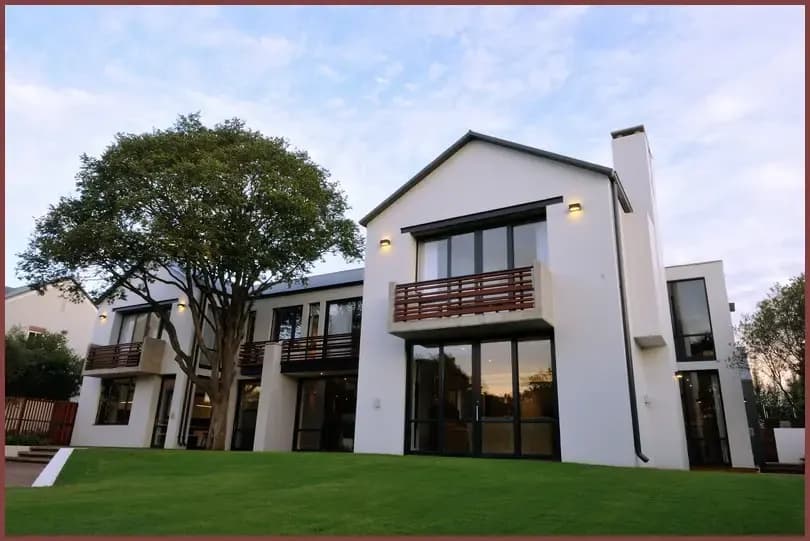 A completed two-storey white house with large aluminium-framed windows and a first-floor balcony