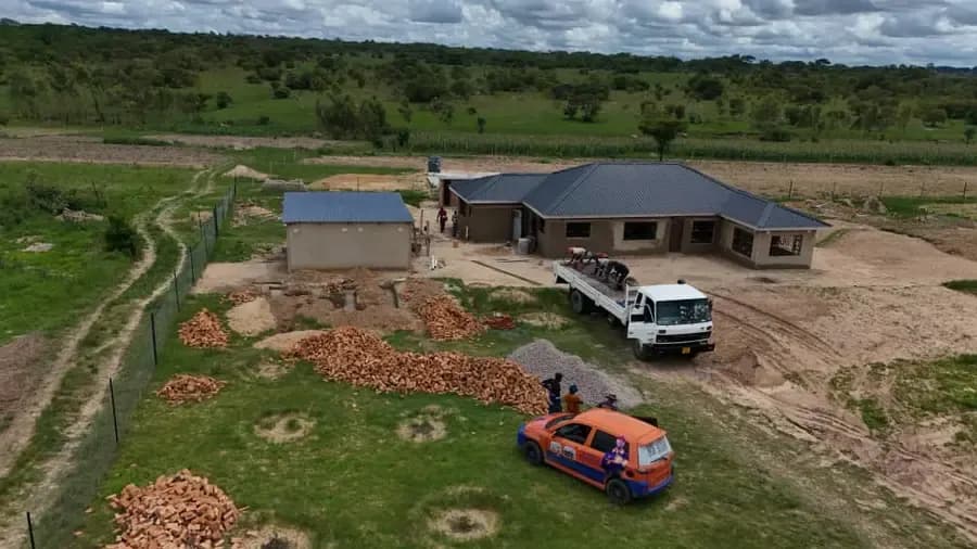 Aerial view of a finished single-storey house with a dark roof, a delivery truck and a bakkie parked on the plot