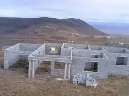 A grey block building under construction on a hillside, with columns cast and a mountain behind