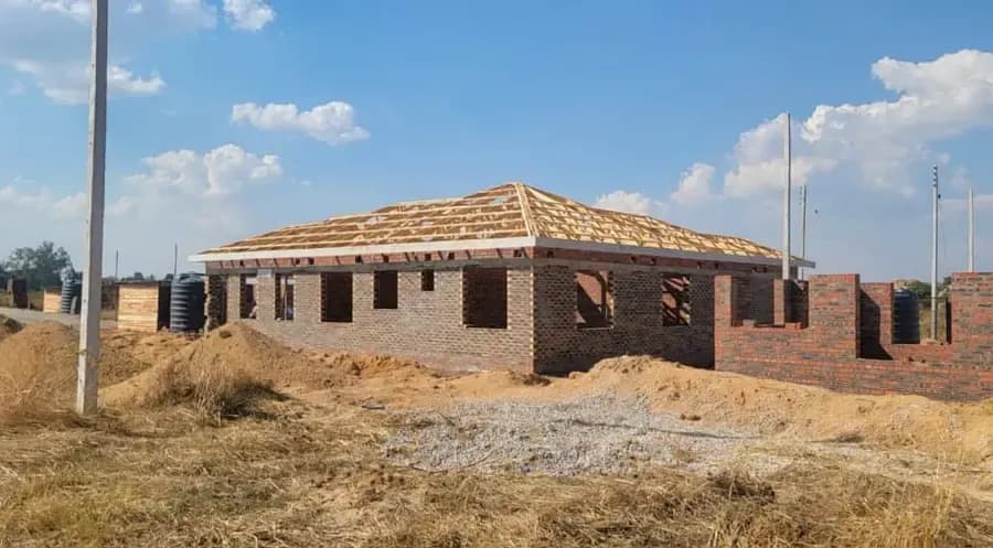 A timber hipped roof structure framed over the brick walls of a house on a dry, open plot